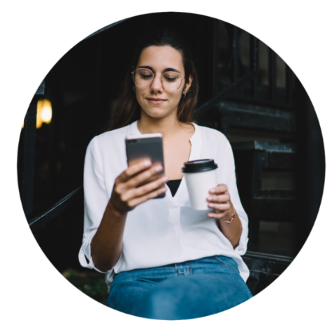 Women in white top wearing glasses drinking coffee whilst using smartphone on the street